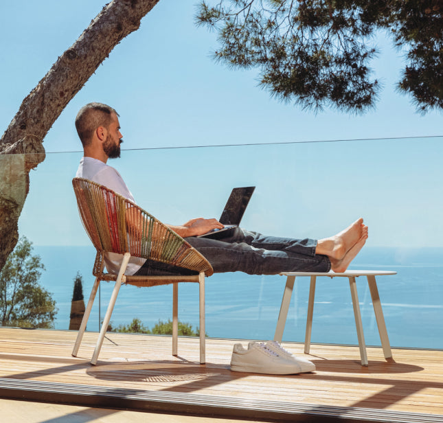 Un homme travaille sur son ordinateur portable en terrasse, face à la mer.
